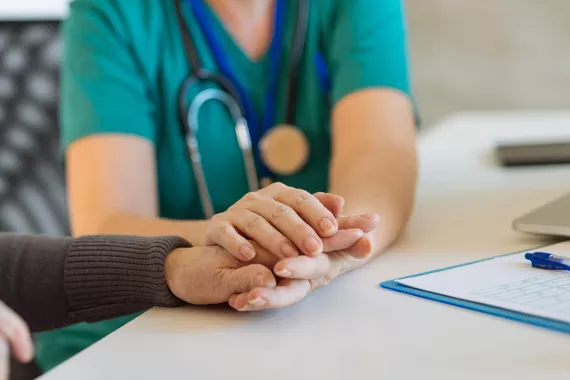 Healthcare professional holding the hands of an elder patient